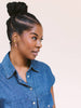 A woman with her hair in a high bun wearing a blue denim shirt, shown in profile against a solid light beige background.