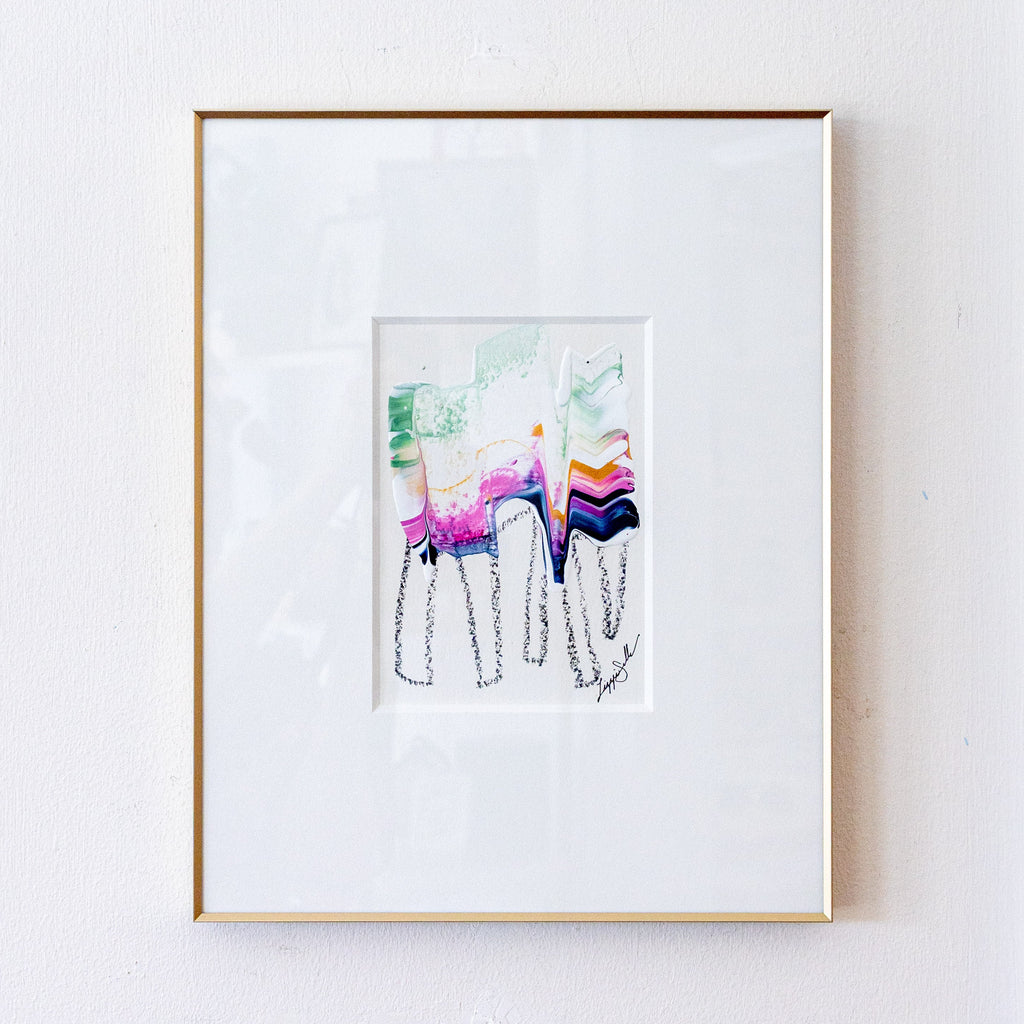 A framed abstract art print featuring colorful brushstrokes and black line drawings, presented in a white mat and a thin gold frame against a white wall.