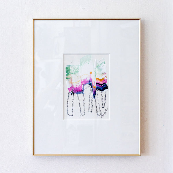 A framed abstract art print featuring colorful brushstrokes and black line drawings, presented in a white mat and a thin gold frame against a white wall.