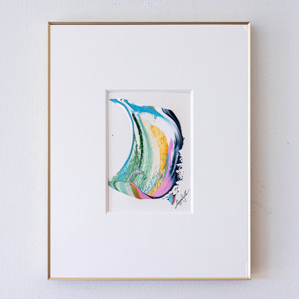 A framed abstract artwork featuring a colorful fluid swirl design in shades of blue, green, yellow, orange, pink, and black, presented in a white mat and a thin gold frame against a white wall.