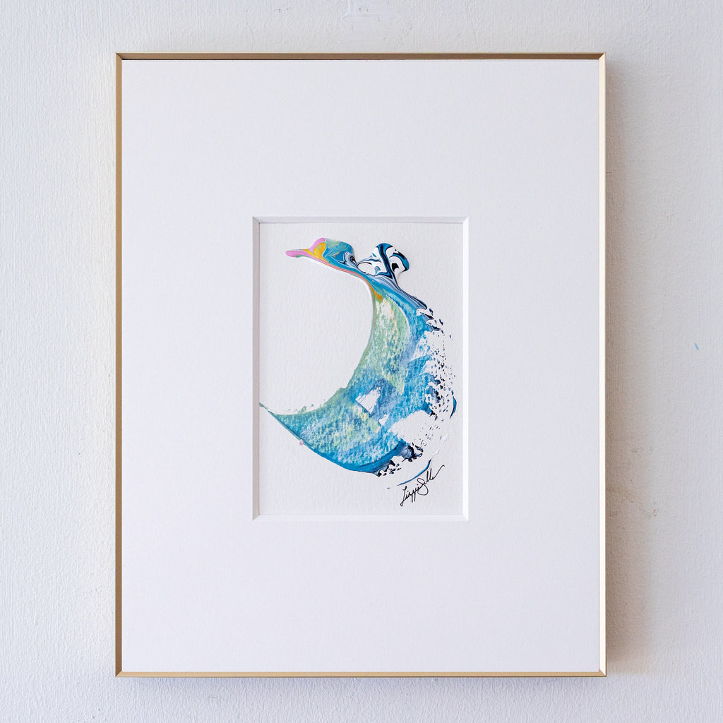 A framed abstract artwork, set in a white mat and a thin gold frame against a white wall.