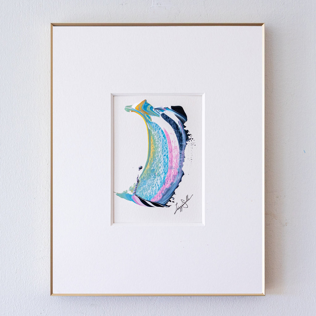 A framed abstract painting, displayed in a white mat with a thin gold frame against a light gray wall.