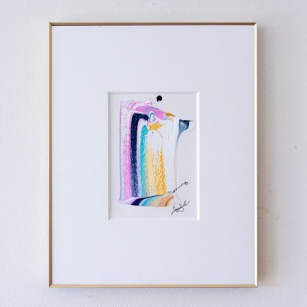 A framed abstract artwork, set within a white mat and a thin gold frame on a light gray wall.