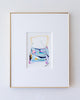 A framed abstract artwork, set in a white mat and a thin gold frame against a light textured wall.