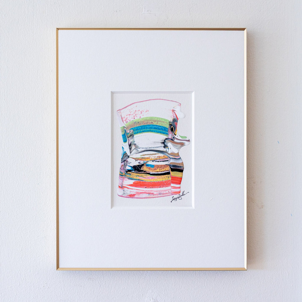 A framed abstract artwork featuring colorful horizontal brushstrokes, presented in a white mat and a thin gold frame against a white wall.
