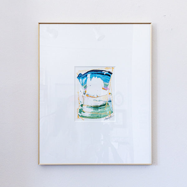 A framed painting featuring a colorful acrylic painting with blue, green, and white tones, set in a white mat and a thin gold frame against a white wall.