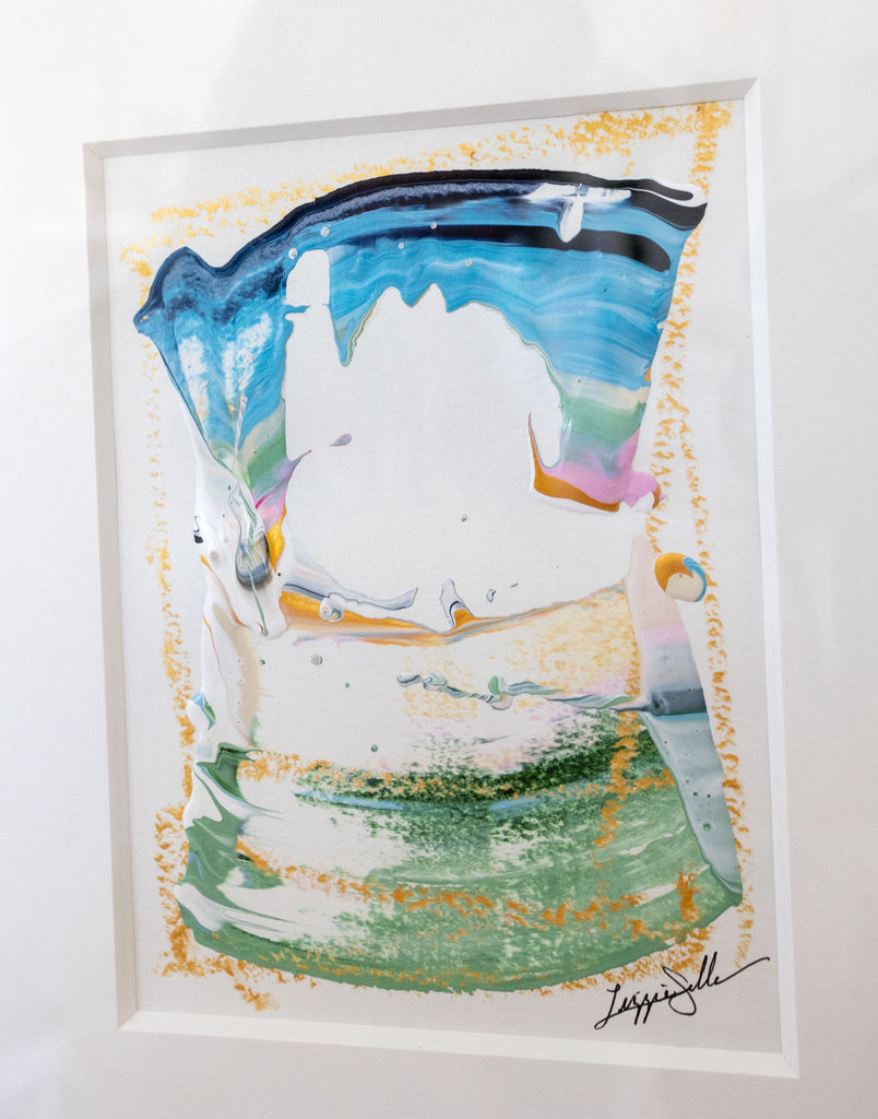 An abstract framed painting featuring a central white shape outlined by flowing blue, green, and gold paint-like textures, with a black signature in the lower right corner.