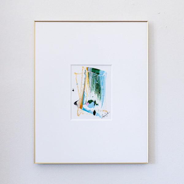 A framed abstract painting featuring green, blue, gold, and black brushstrokes, presented in a white mat and a thin gold frame against a white wall.