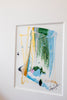 A framed abstract painting featuring a stylized boot illustration with green, blue, yellow, pink, and black paint strokes on a white background, hung on a white wall.