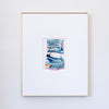 A framed abstract painting featuring textured blue, green, and pink brushstrokes, presented in a white mat and a thin gold frame against a light gray wall.