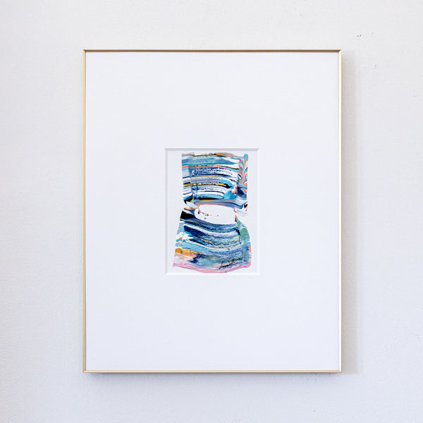 A framed abstract painting featuring textured blue, green, and pink brushstrokes, presented in a white mat and a thin gold frame against a light gray wall.