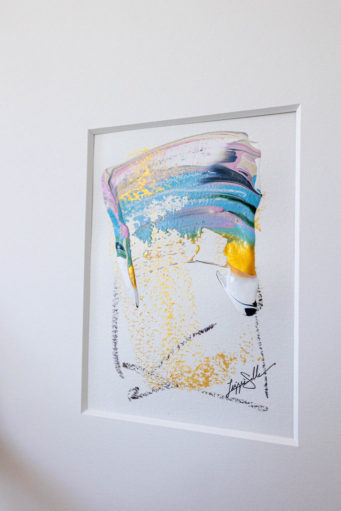 A framed abstract painting featuring blue, metallic gold, light pink, and black oil pastel markings, presented in a white mat.