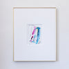 A framed abstract painting featuring colorful vertical brushstrokes in pink, blue, and teal on a white mat, enclosed in a thin gold frame against a light gray wall.
