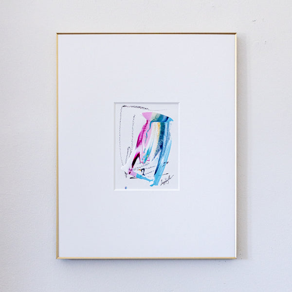 A framed abstract painting featuring colorful vertical brushstrokes in pink, blue, and teal on a white mat, enclosed in a thin gold frame against a light gray wall.