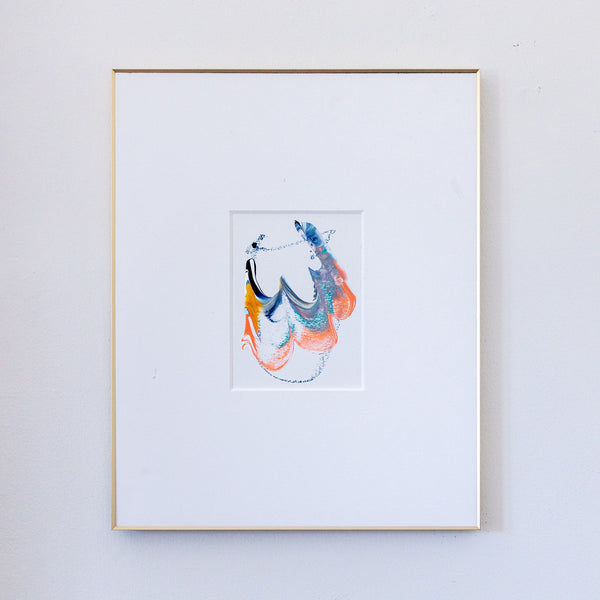 A framed abstract painting featuring blue, coral, blue, gold, and black in a white mat, enclosed in a thin gold frame against a light gray wall.