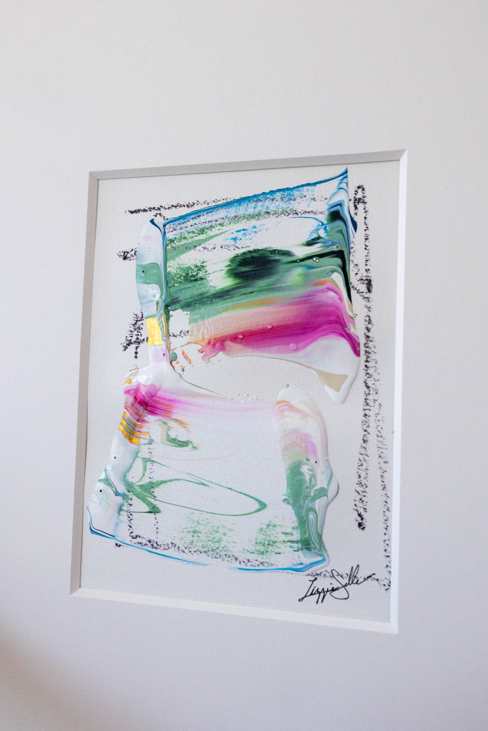 An abstract framed painting featuring fluid, layered paint textures in green, pink, blue, and white, mounted on a plain white wall.