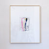 A framed abstract painting featuring pastel pink, yellow, blue, and black brushstrokes on a white mat, enclosed in a thin gold frame and hung on a light gray wall.