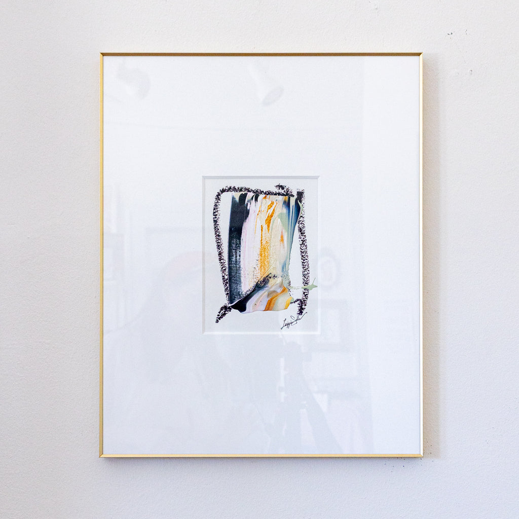 A framed abstract painting featuring black, metallic gold, light pink acrylic with black oil pastel, presented in a white mat and a thin gold frame against a light gray wall.