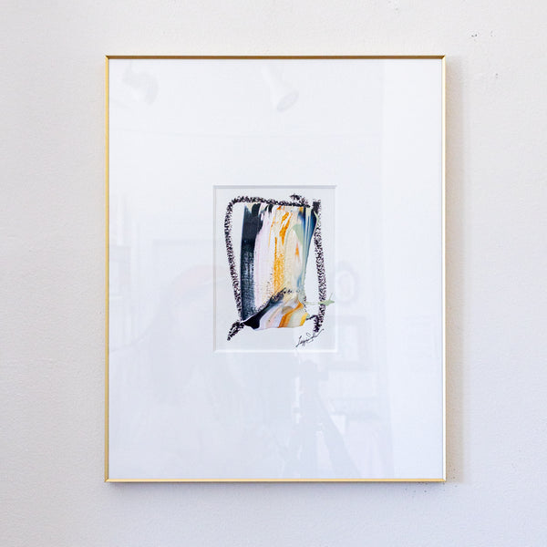 A framed abstract painting featuring black, metallic gold, light pink acrylic with black oil pastel, presented in a white mat and a thin gold frame against a light gray wall.