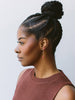 A woman in profile wearing a rose-brown ribbed knit top and a single dangling pink beaded earring against a light gray background.
