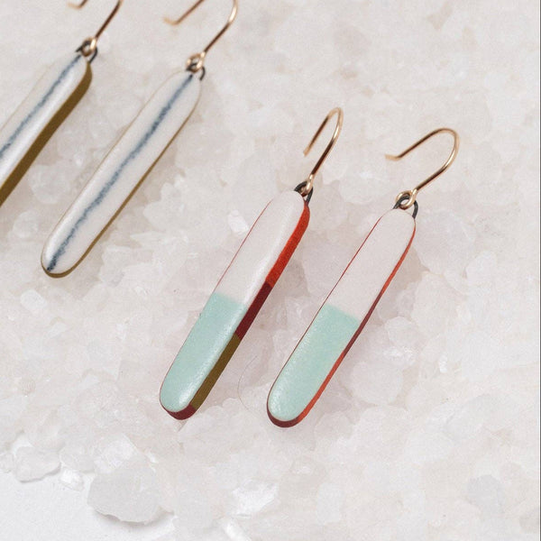 Three dangle earrings with elongated rectangular charms in different color combinations, displayed on a bed of white sea salt. The earrings feature gold-tone fishhook wires and charms with a silver-and-white split design, a red-and-white split design, and a mint-green-and-white split design.