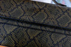 Close-up of a snakeskin-patterned handbag in olive green and black, showing the textured scale pattern and a black leather trim.