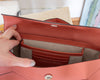 A close-up of a terracotta-colored pebbled leather clutch bag being held open by a hand, showing its interior card slots and beige lining.