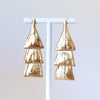 Pair of bronze earrings on a white stand against a light gray background