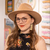 Woman wearing a beige hat, bronze statement earrings, and floral dress in an art gallery setting
