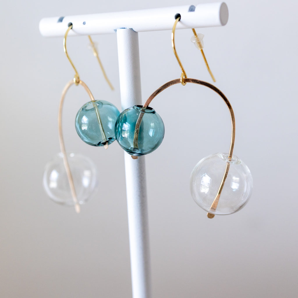 Earrings with blue glass beads and gold accents on a white stand against a light gray background