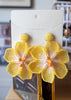 Yellow floral beaded earrings on a branded card with a blurred background
