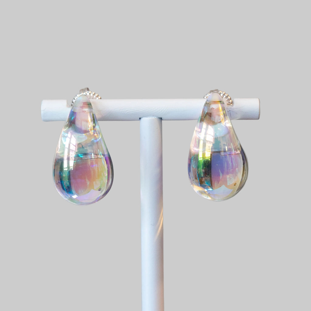 Teardrop-shaped earrings on a white stand with a blurred background