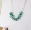 A delicate gold wire necklace with translucent light blue-green beads, draped on a white wooden display stand.
