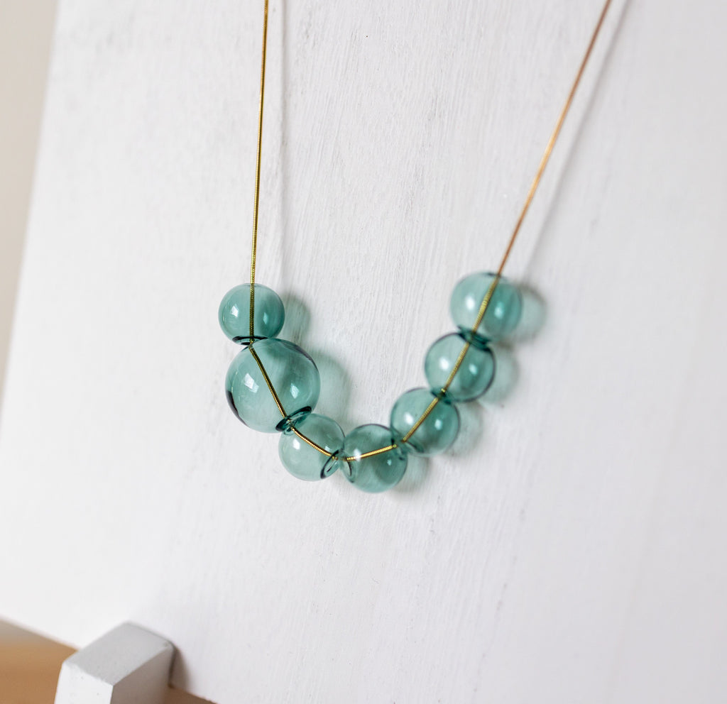 A delicate gold wire necklace with translucent light blue-green beads, draped on a white wooden display stand.