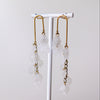 A pair of long dangle earrings with gold-toned metal hooks and translucent white flower-shaped beads, displayed on a white jewelry stand against a soft light gray background.