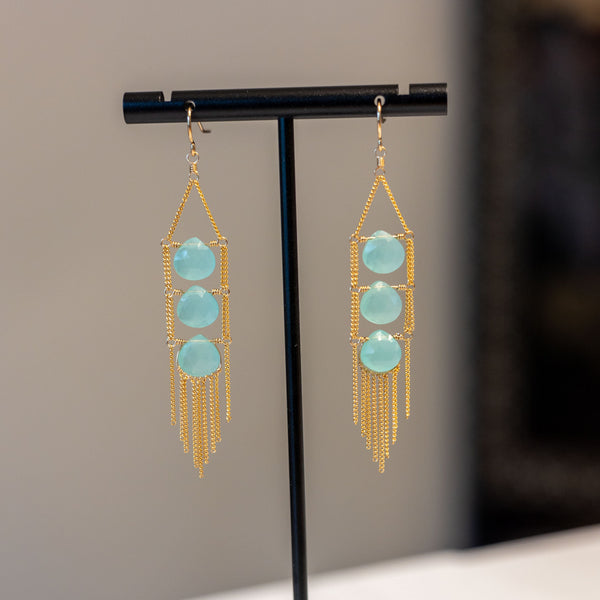 Gold and turquoise earrings on a black stand against a neutral background