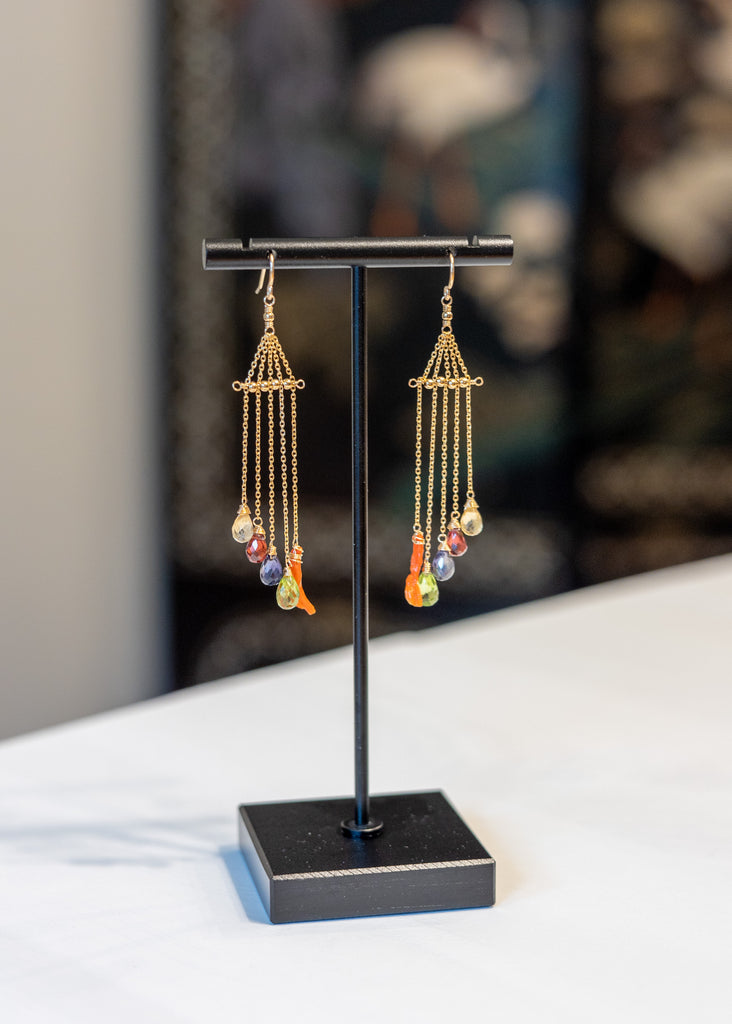 Pair of gold-framed earrings with colorful beads on a black stand.