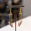 Gold earrings with colorful beads on a black stand against a blurred background