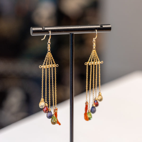 Gold earrings with colorful beads on a black stand against a blurred background