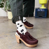 Person wearing maroon clogs with wooden soles and black and white socks with black polka dots.