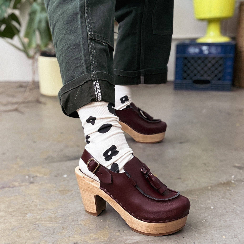 Person wearing maroon clogs with wooden soles and black and white socks with black polka dots.