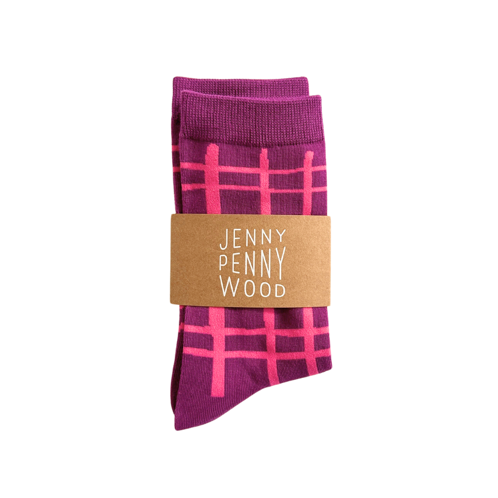 A pair of folded purple socks with a pink plaid pattern, wrapped in a brown paper band that reads 'JENNY PENNY WOOD' in white text, on a solid white background.