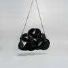 A black textured shoulder bag with a unique, organic, flower-like layered design and a silver chain strap, photographed against a neutral light gray background.