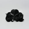 A black textured leather clutch bag with a unique accordion or flower-like petal design, photographed on a neutral light gray background.