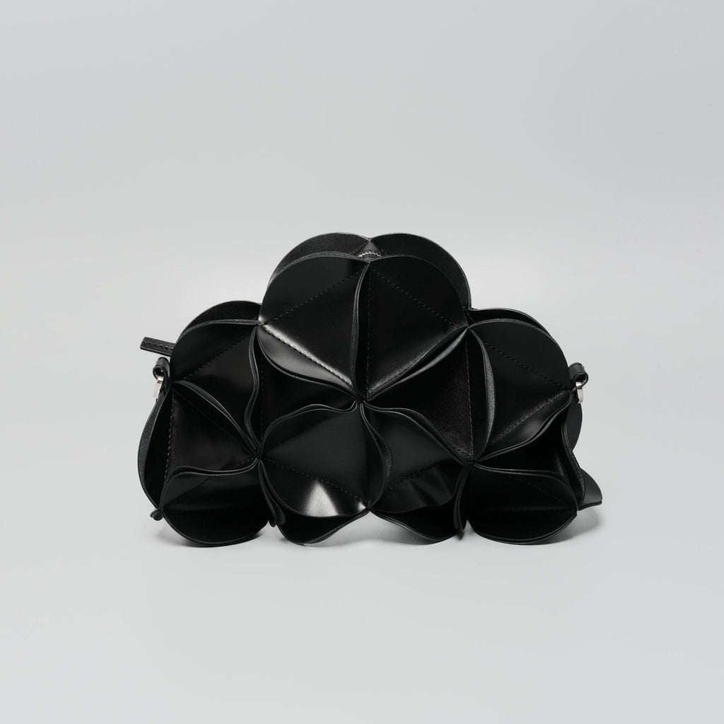 A black textured leather clutch bag with a unique accordion or flower-like petal design, photographed on a neutral light gray background.