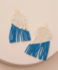 Pair of beaded earrings with blue and white fringes on a beige surface