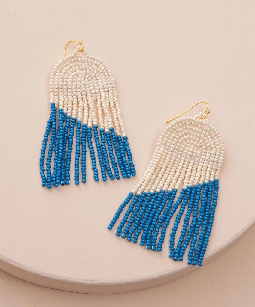 Pair of beaded earrings with blue and white fringes on a beige surface