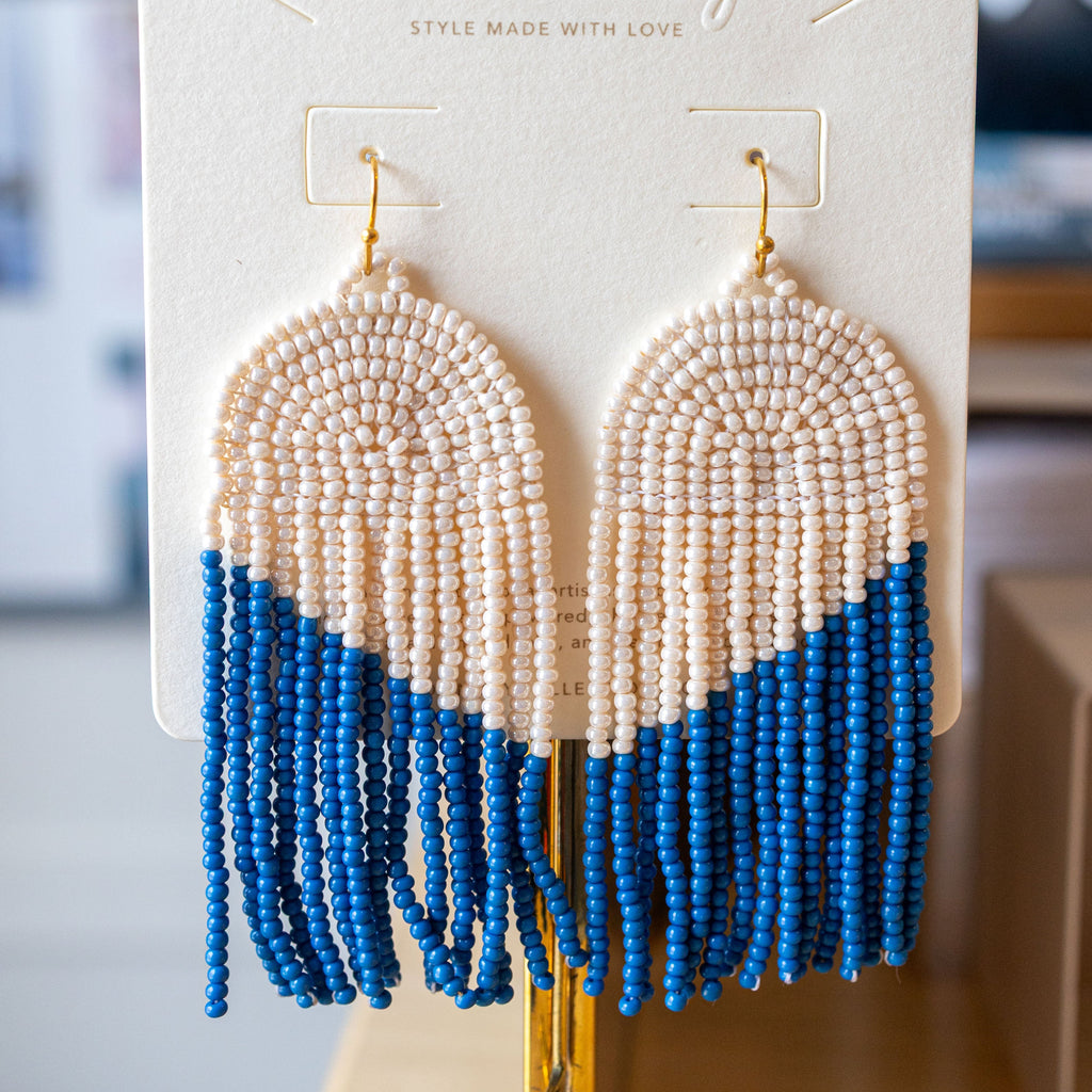 Pair of beaded earrings with blue fringe on a branded earring card.