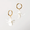 Gold hoop earrings with white floral charms on a light gray background