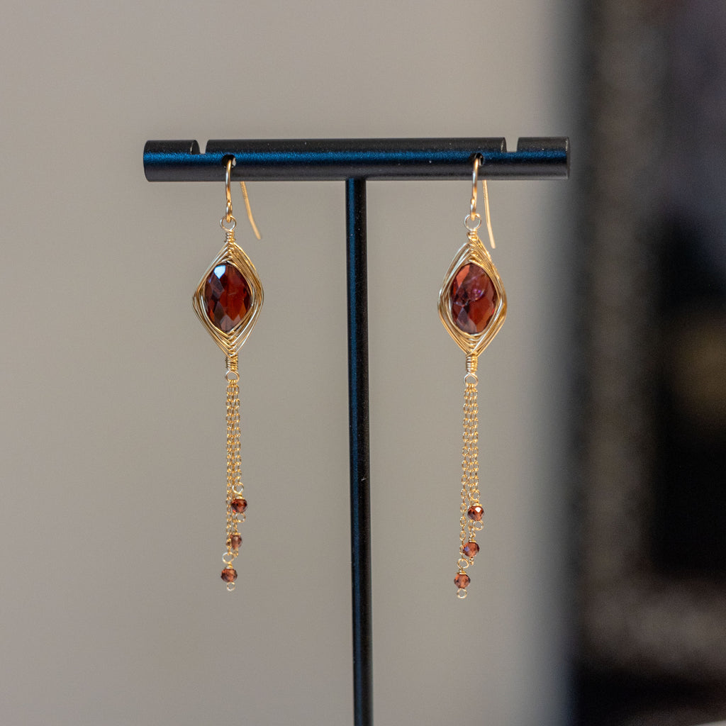 Pair of earrings on a black stand against a neutral background